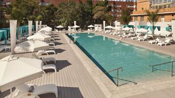 Un espace piscine doté de chaises longues et de parasols, entouré d’immeubles.