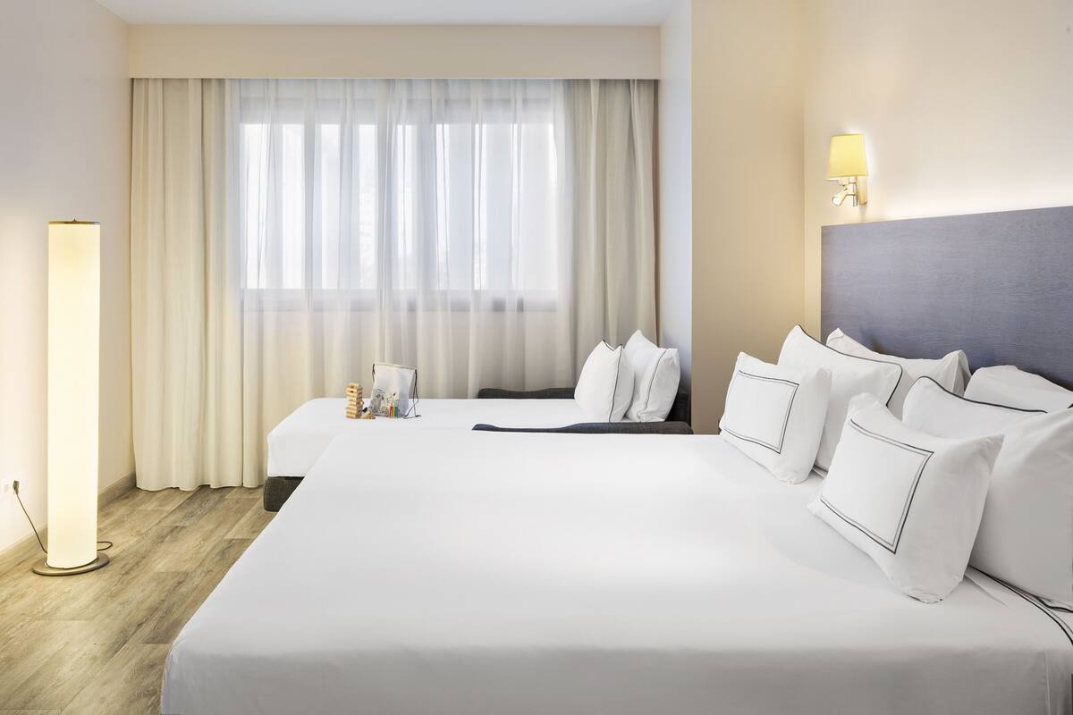 A hotel room with a large bed, a bedside table, a lamp, and a window with curtains.