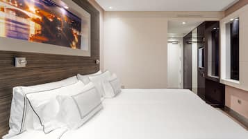 Una habitación de hotel moderna con una cama grande, un cuadro con vista nocturna y un pasillo que conduce a un baño.