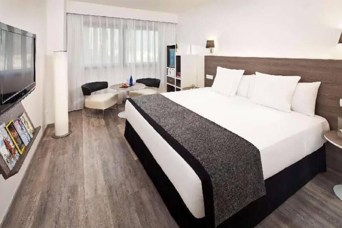 A hotel room with a large bed, a TV, a desk with a chair, and a window with curtains.