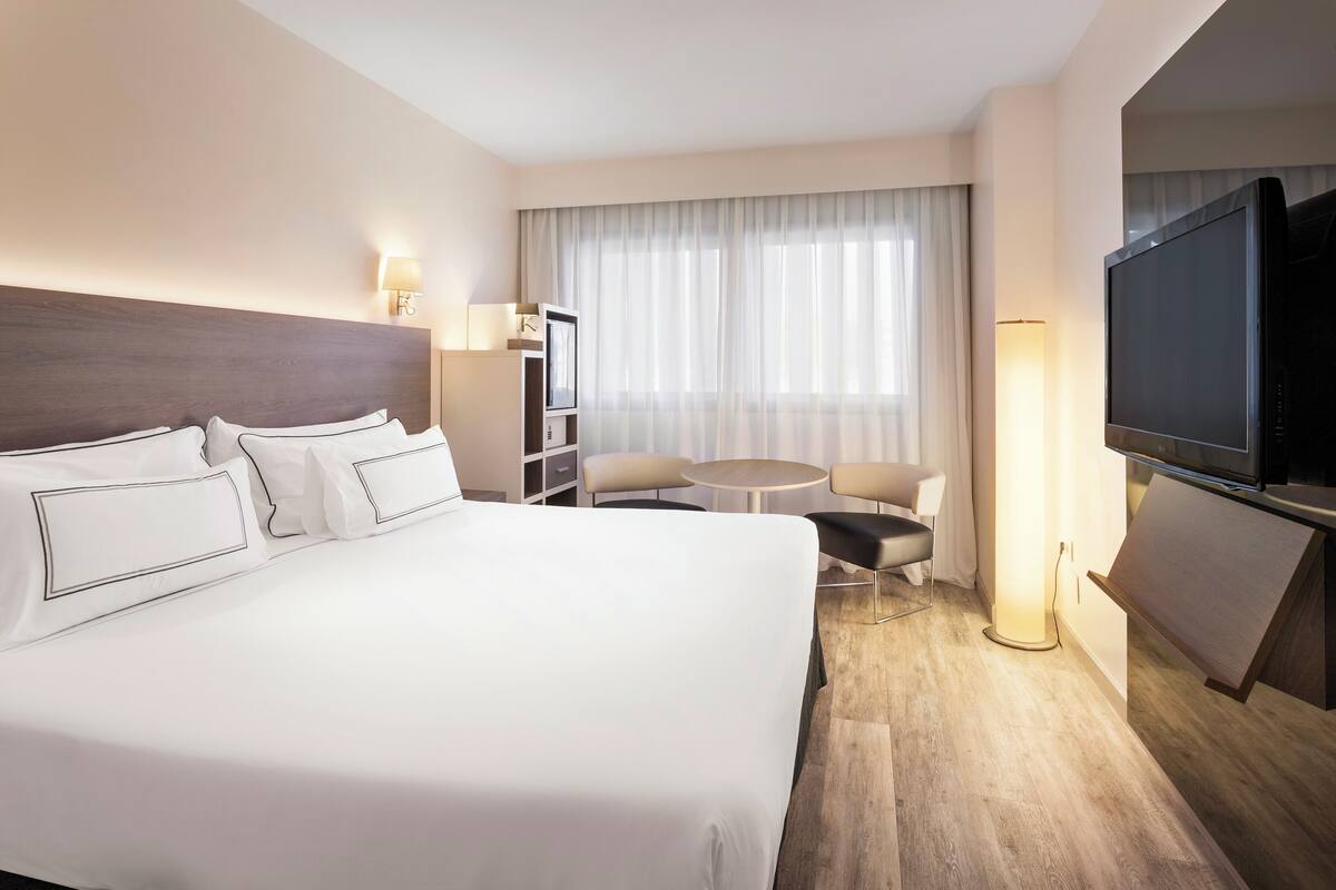 A hotel room with a large bed, a TV, a desk, and a chair.