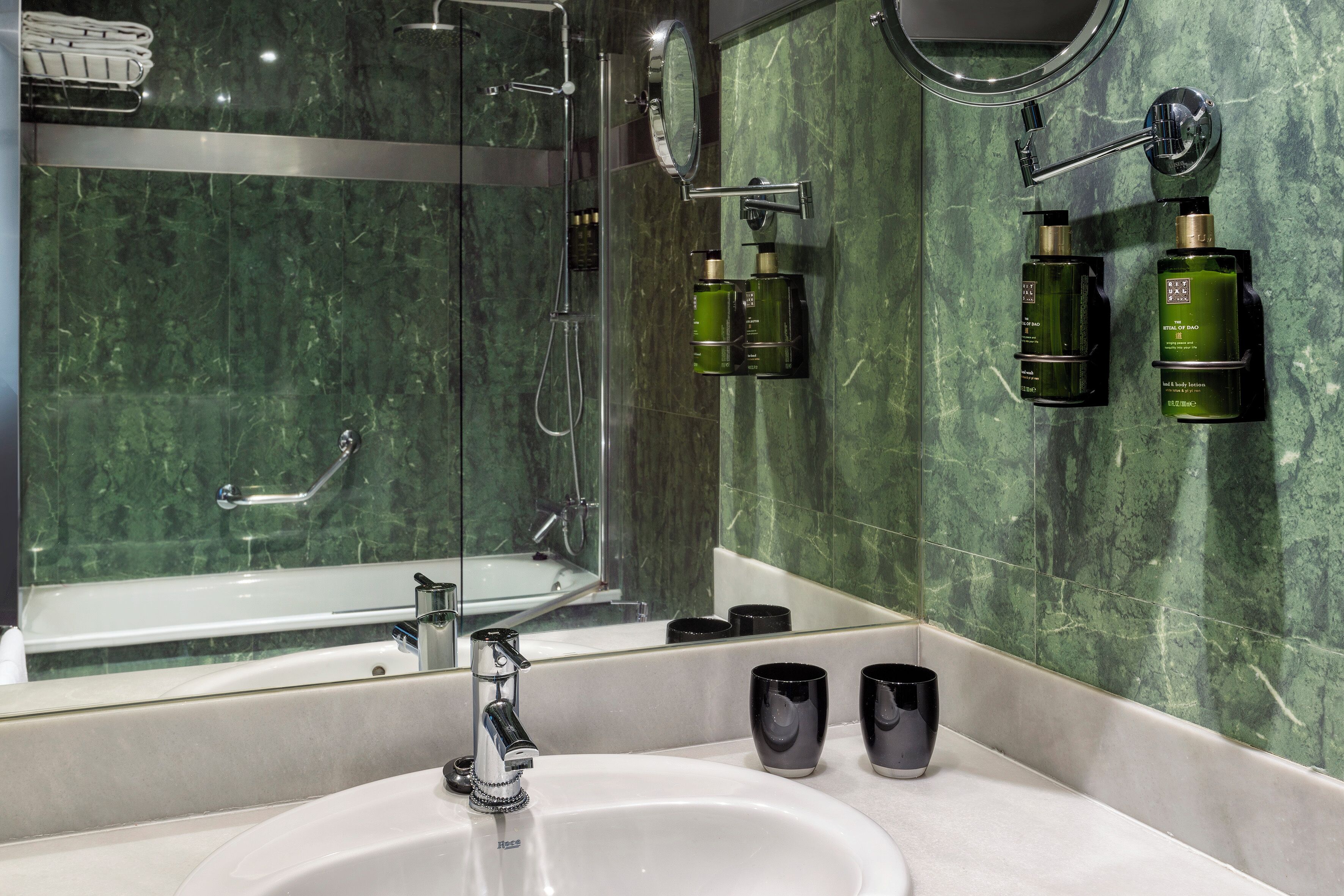 A modern bathroom with a glass-enclosed shower, a large mirror, and a sink with two black cups.