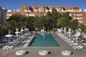 A swimming pool with lounge chairs and umbrellas, surrounded by trees and buildings. - Melia Lebreros (Seville)