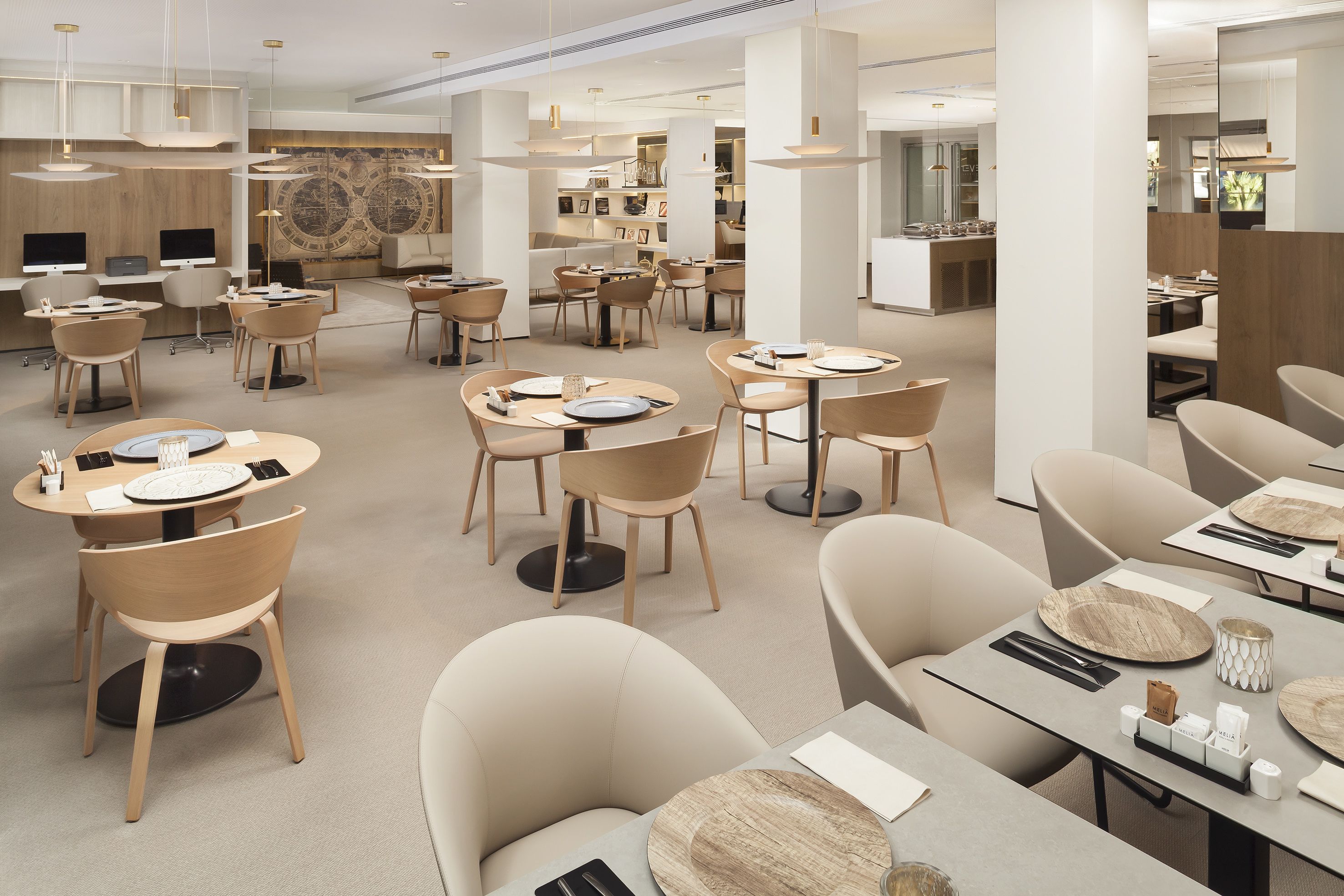 Un restaurante moderno con mesas redondas, sillas color beige e iluminación colgante.