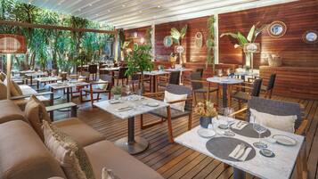 Un restaurante con suelo de madera, mesas dispuestas con vajilla y plantas en macetas.