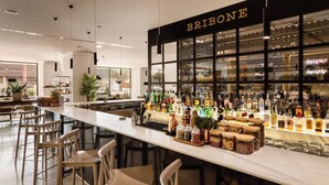 Zona de bar con taburetes, una barra con botellas y un cartel que dice 'BRIBONE'.