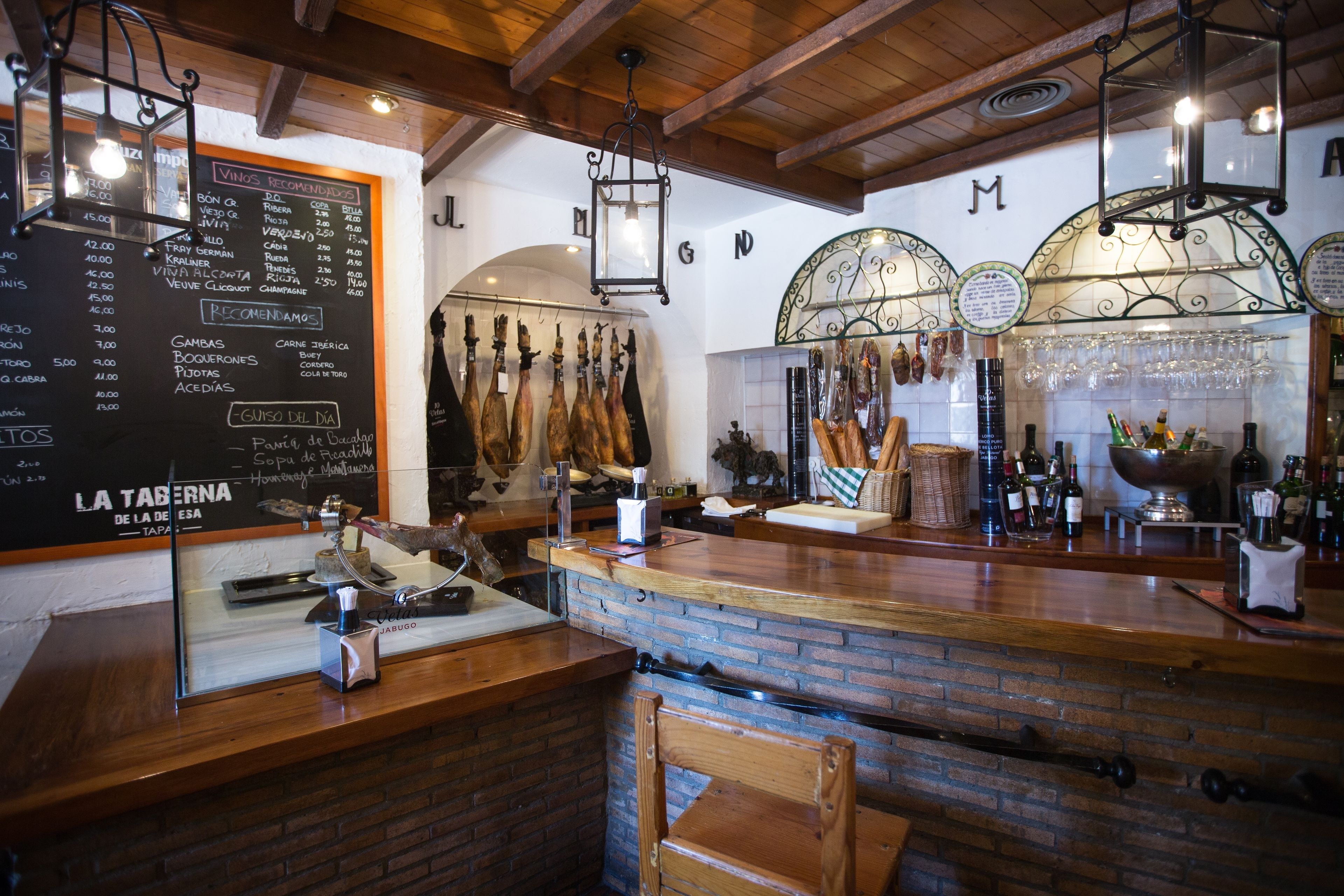 Zona de bar con una pizarra de menú, carnes colgando y una variedad de botellas.