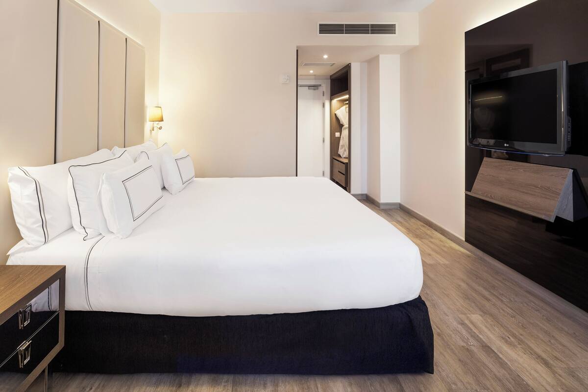 A modern hotel room with a large bed, a TV, and a walk-in closet.