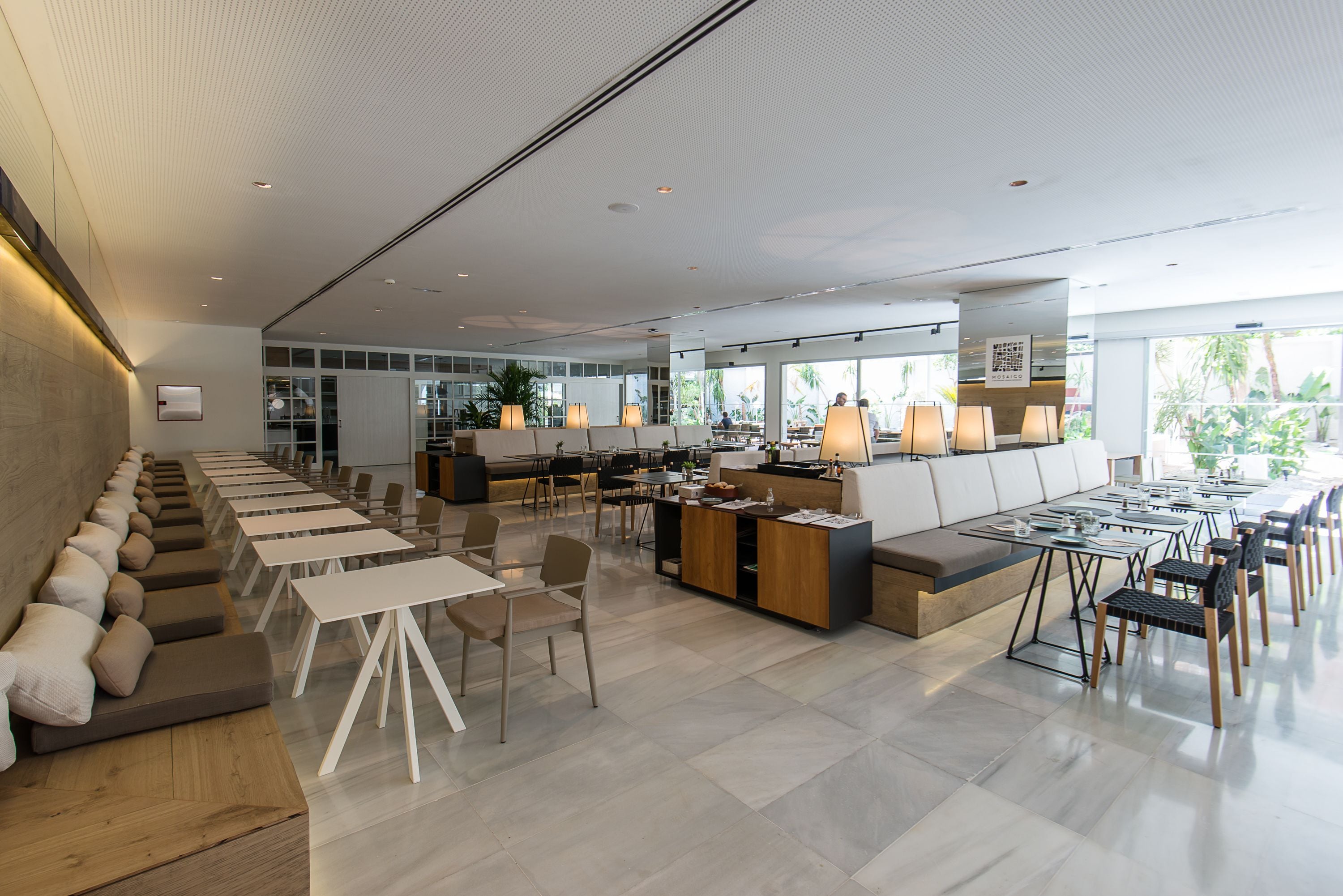 Un amplio y moderno salón con asientos largos, un mostrador de recepción y una zona de bar.
