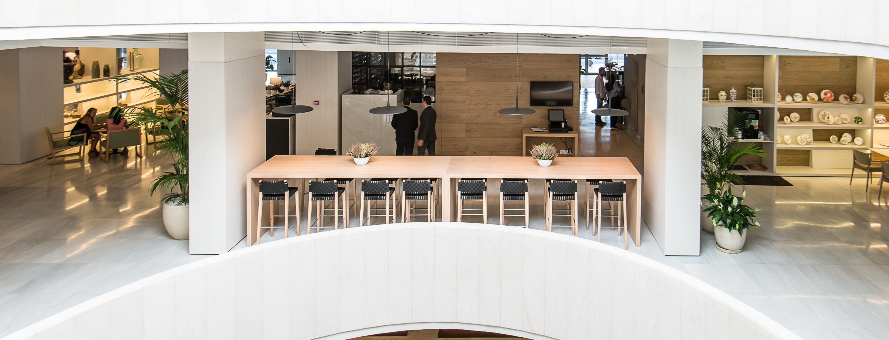 Un espace bar moderne, doté d’un long comptoir et de nombreux tabourets, entouré d’étagères où sont exposés des objets décoratifs.