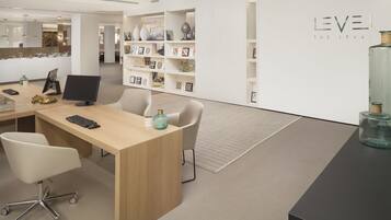 A modern office space with a wooden desk, two chairs, a computer monitor, and a bookshelf filled with decorative items.