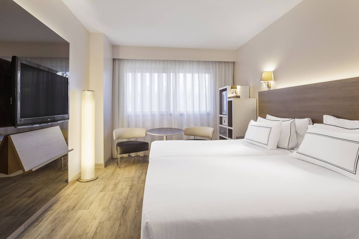 A hotel room with a large bed, a TV, a desk, a chair, and a lamp.