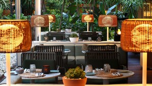 Un área de comedor al aire libre con lámparas de mimbre, asientos acolchados y plantas en macetas.