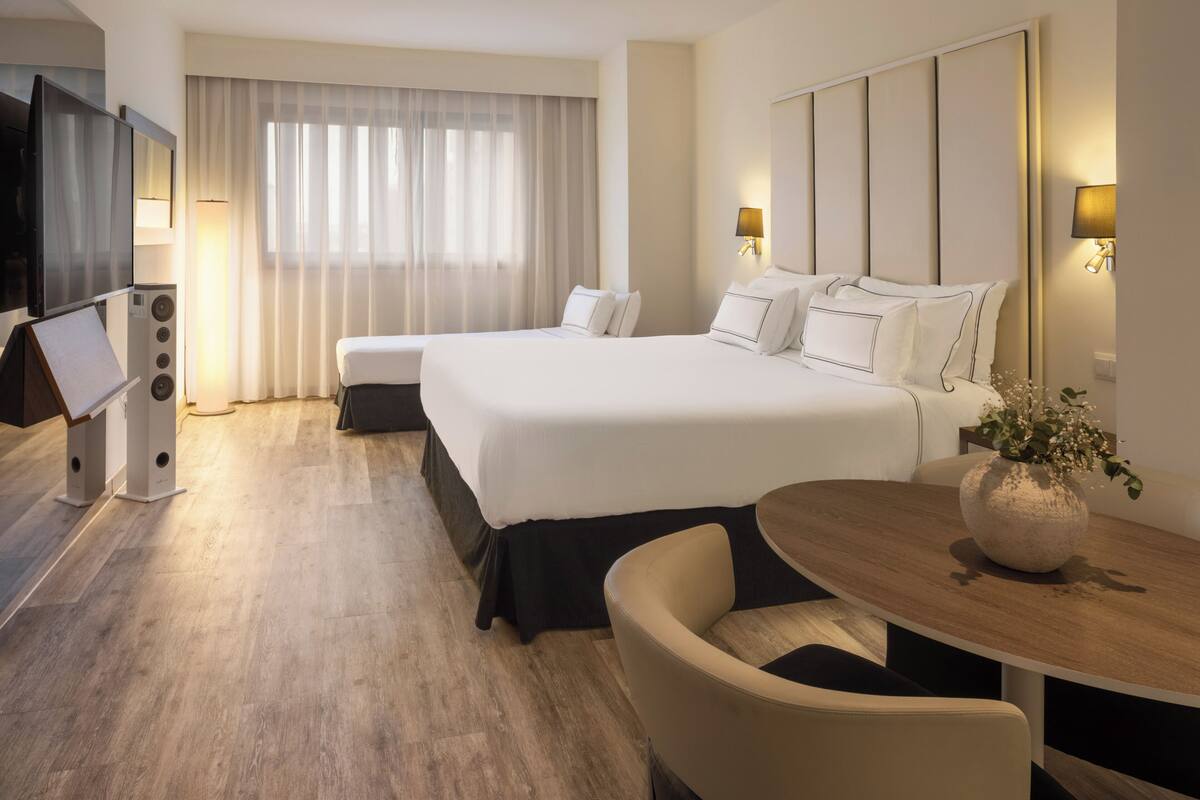 A hotel room with a large bed, a desk, a chair, a TV, and a window with curtains.