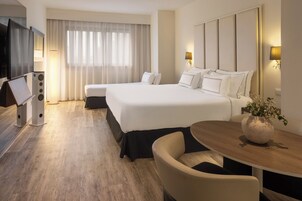 A hotel room with a large bed, a desk, a chair, a TV, and a window with curtains.