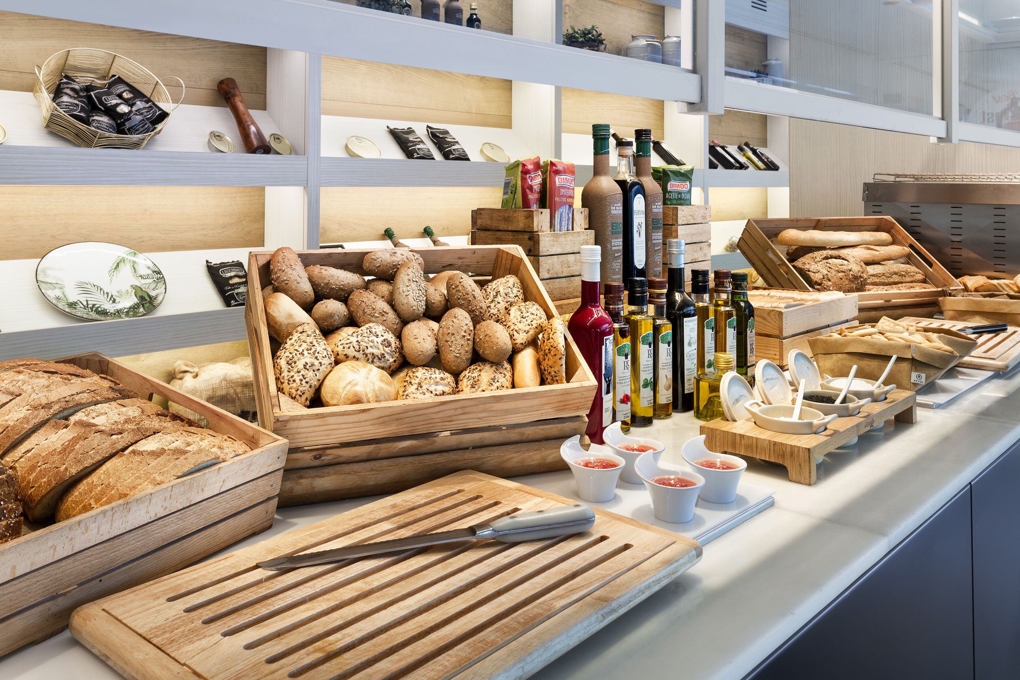 Mostrador de panadería con panes y pasteles diversos, botellas de aceite de oliva y condimentos.