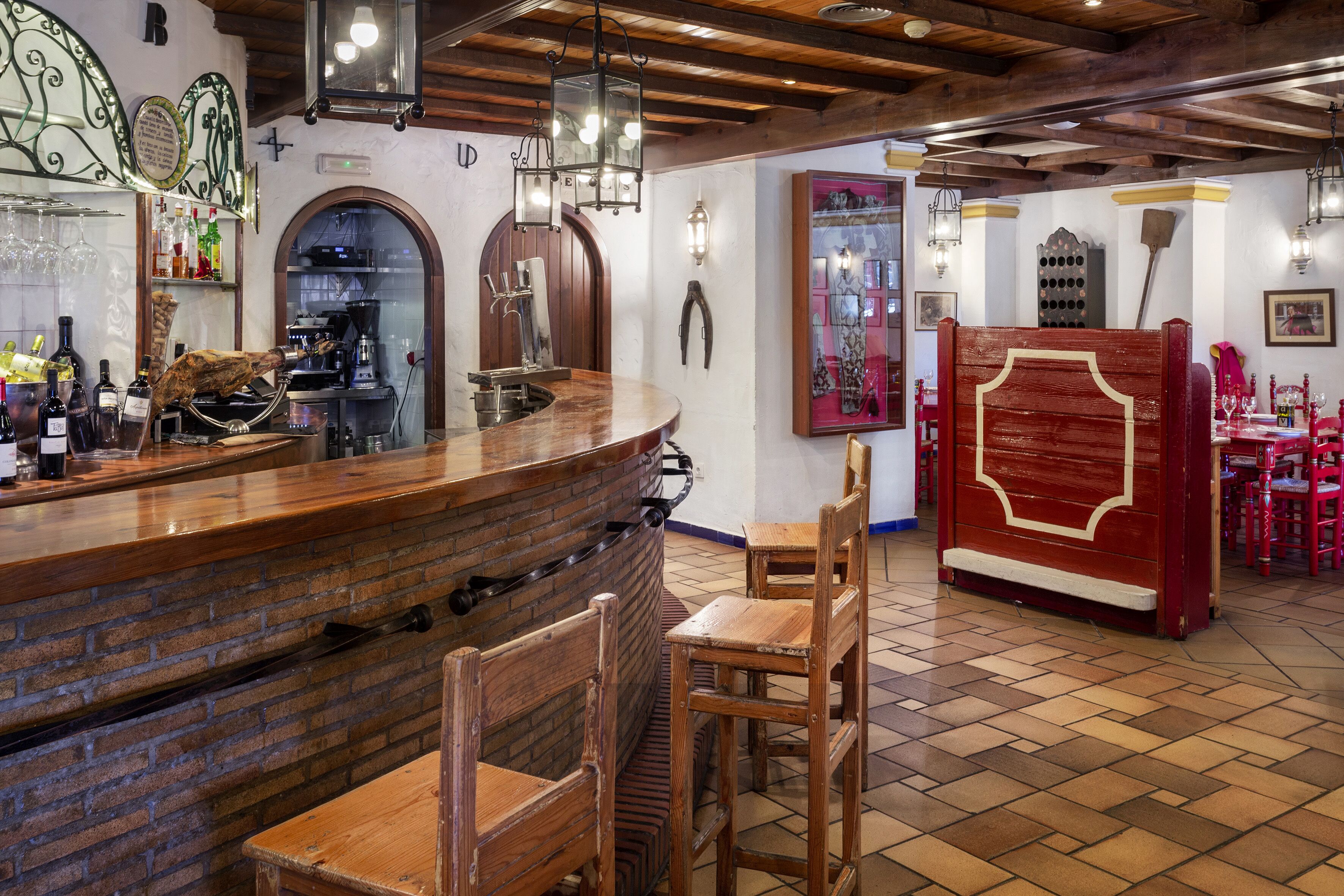 Un espace bar avec un comptoir en briques, des chaises en bois et un séparateur rouge.