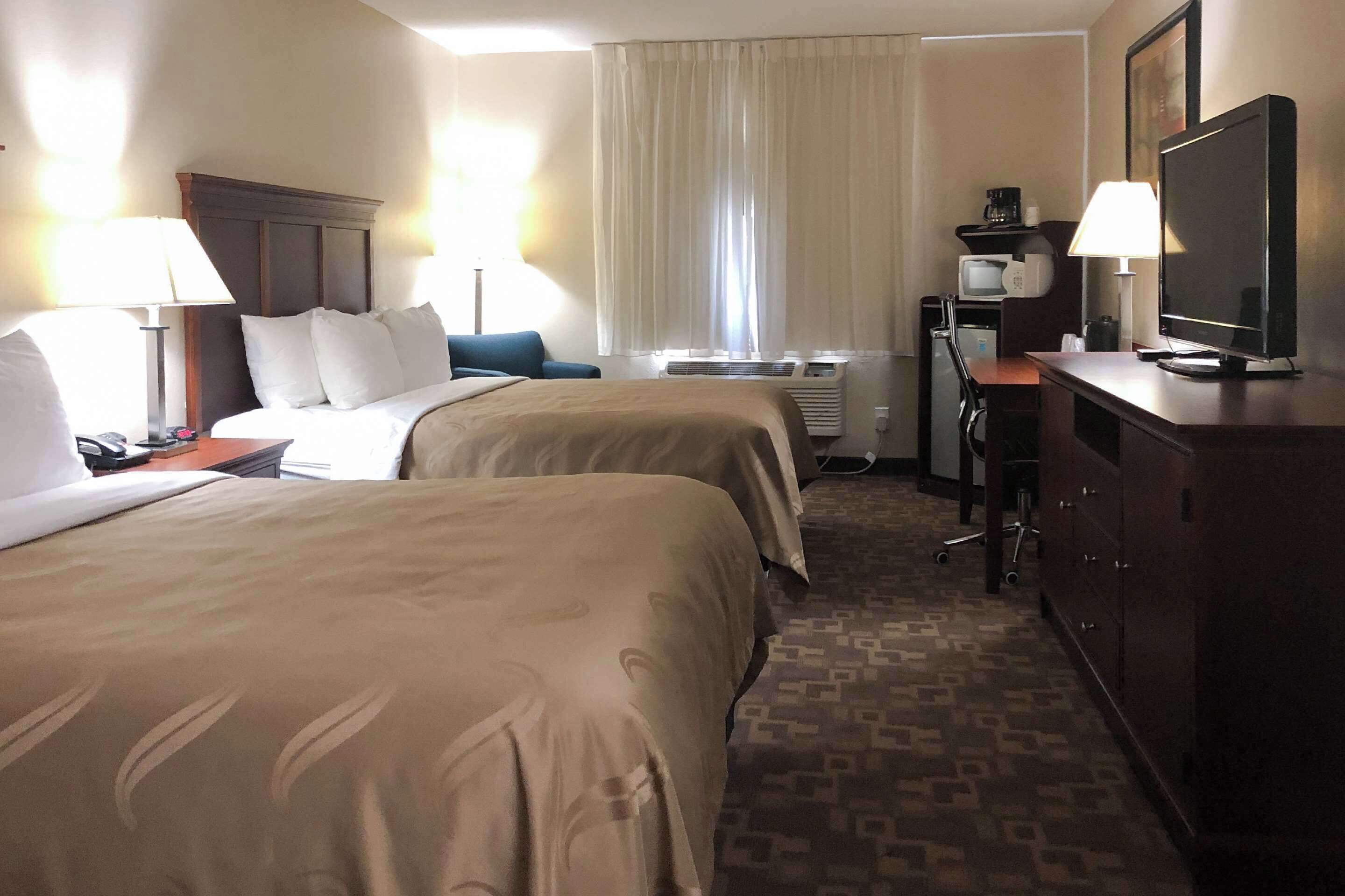 Une chambre d’hôtel avec deux lits, un bureau avec une télévision, une lampe de bureau, un four à micro-ondes et un appareil de climatisation.