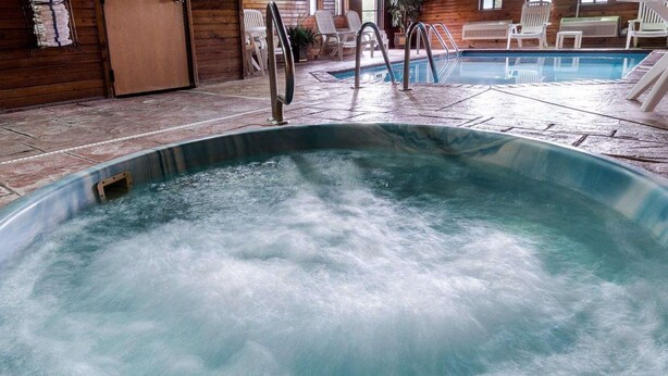 Un bain à remous avec un escalier en métal, entouré de chaises d’extérieur et d’une terrasse en bois.