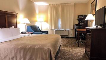 A hotel room with a large bed, two bedside lamps, a desk with a computer, a chair, and a dresser.