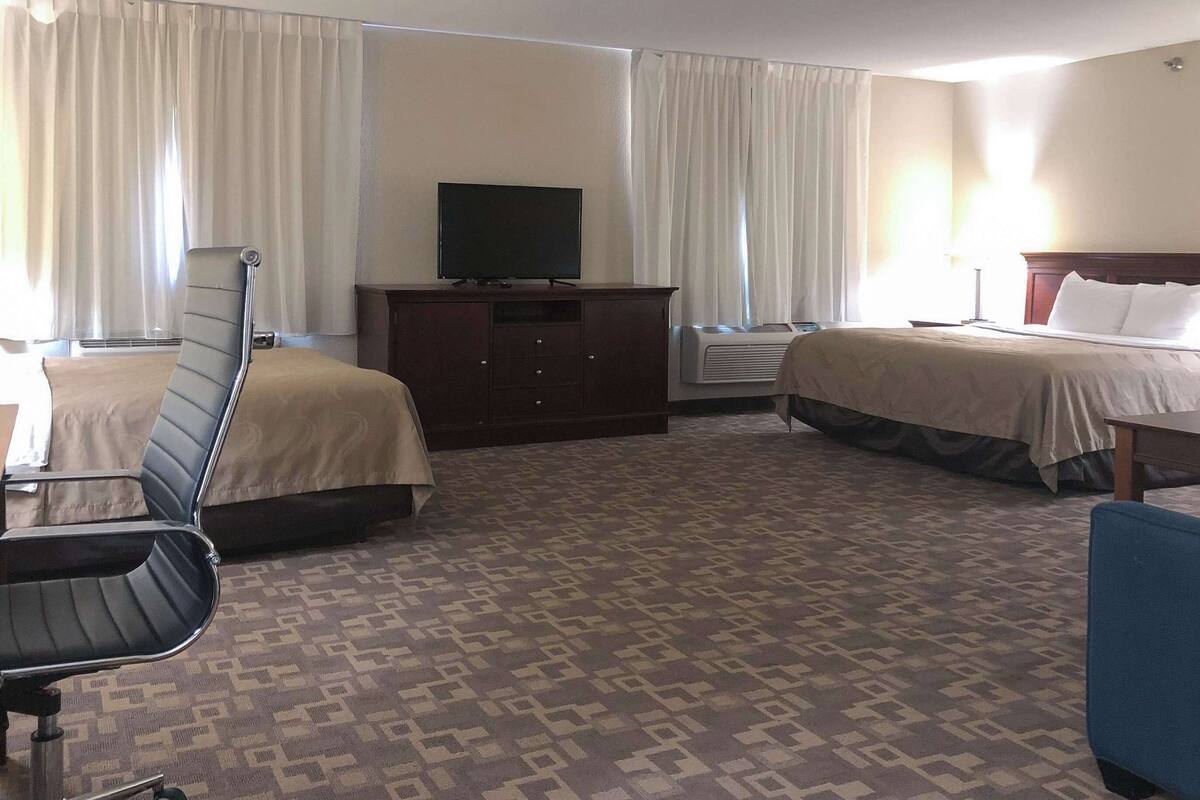 A hotel room with two beds, a desk, a chair, a television, and an air conditioning unit.