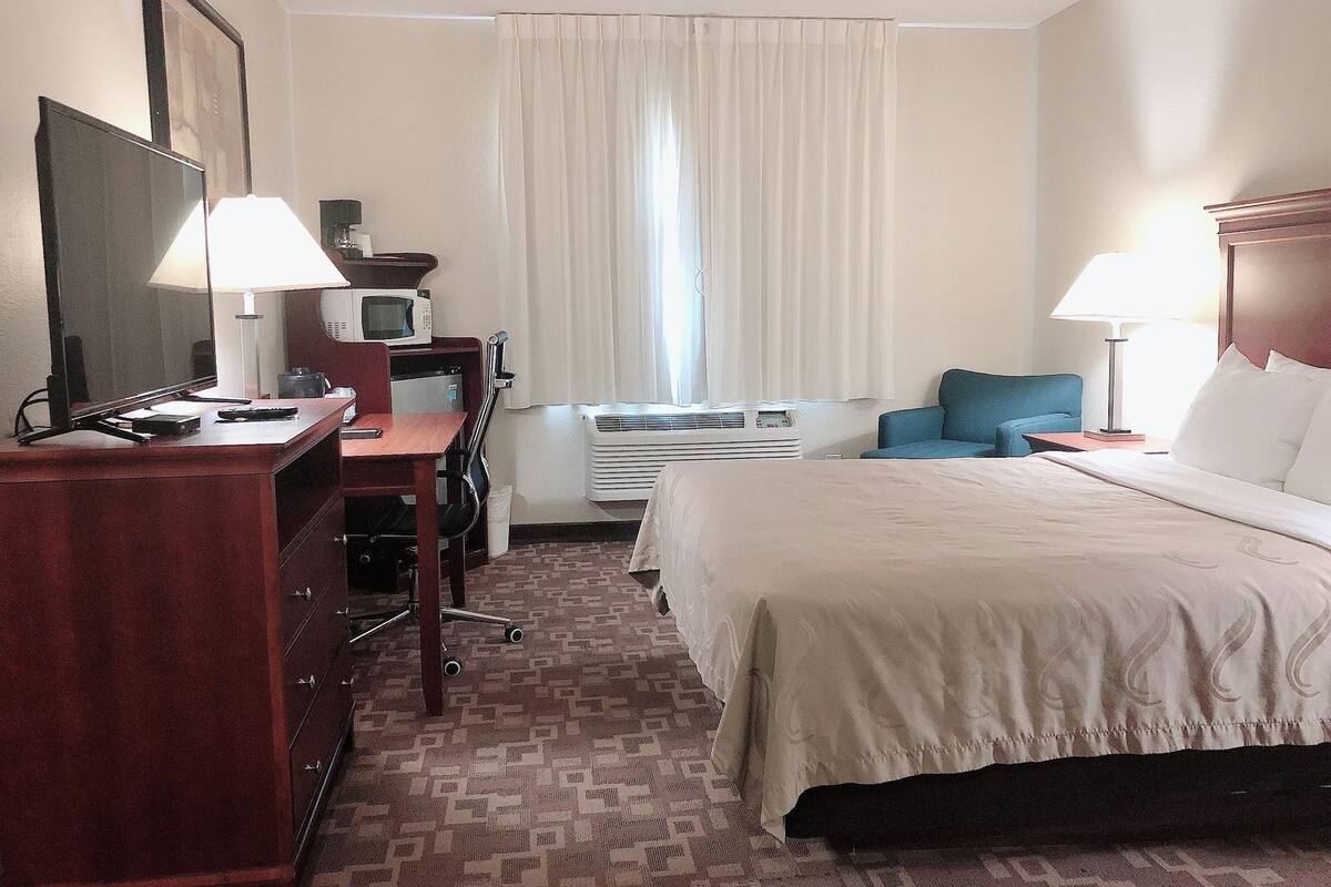 A hotel room with a bed, desk, chair, TV, and a window with curtains.