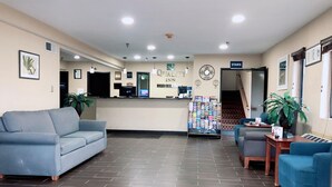 Un hall d’hôtel avec un comptoir d’accueil, un canapé bleu, une petite table avec une plante et un escalier.