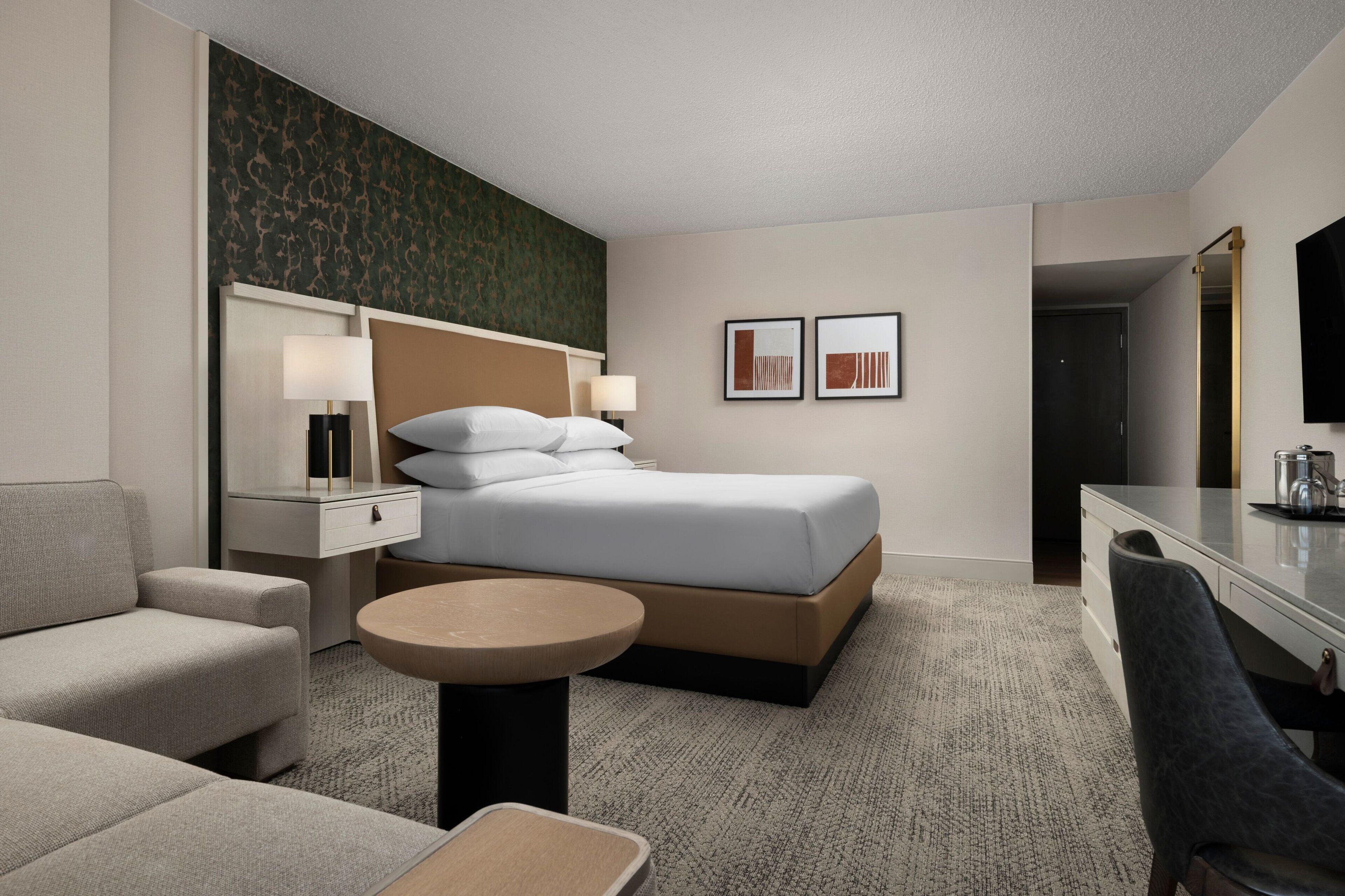 Una habitación de hotel con una cama, un escritorio, una silla, una mesita y un televisor.