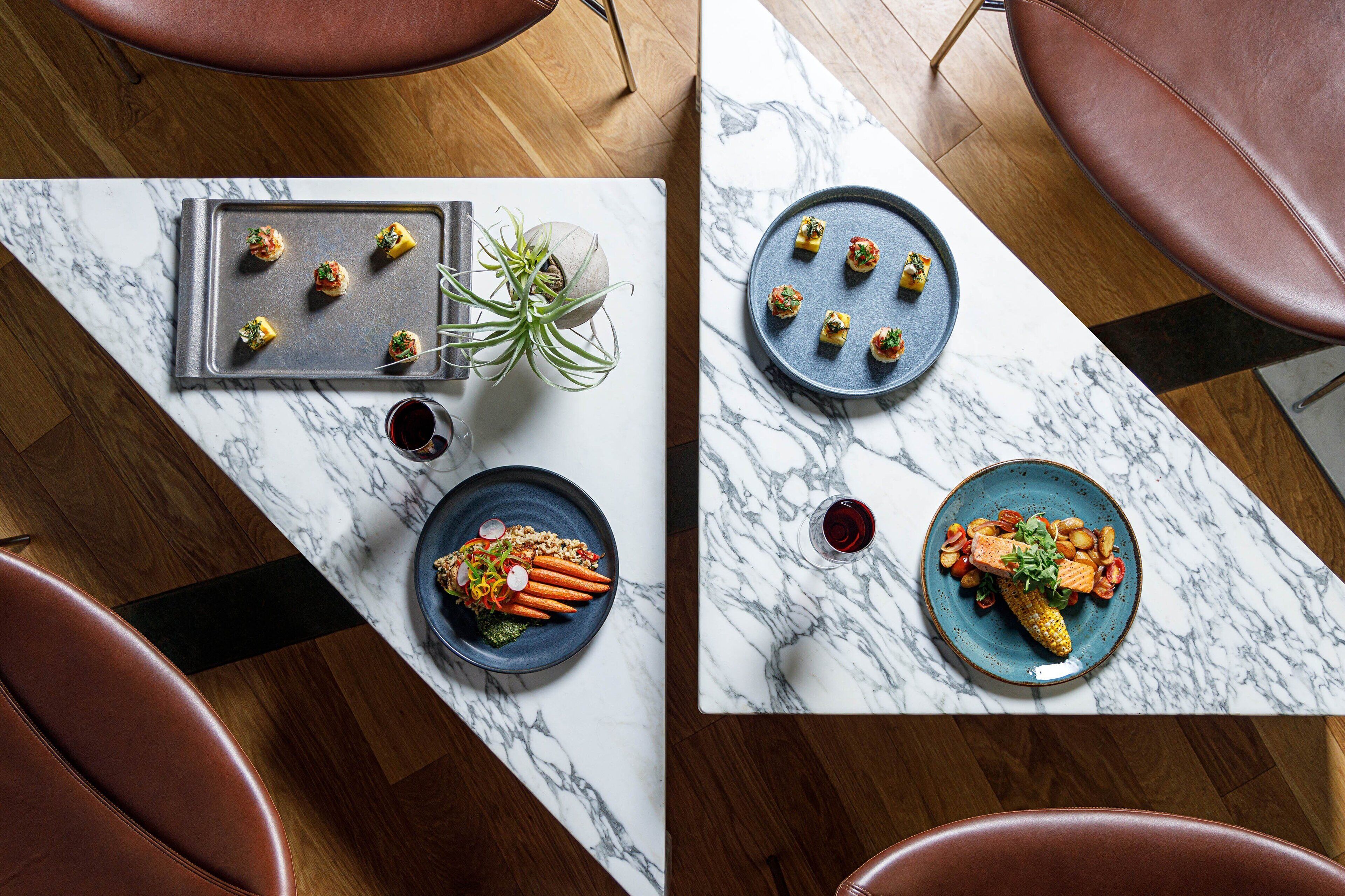 A dining area with a marble table, two plates of food, a plant, and a wine glass.