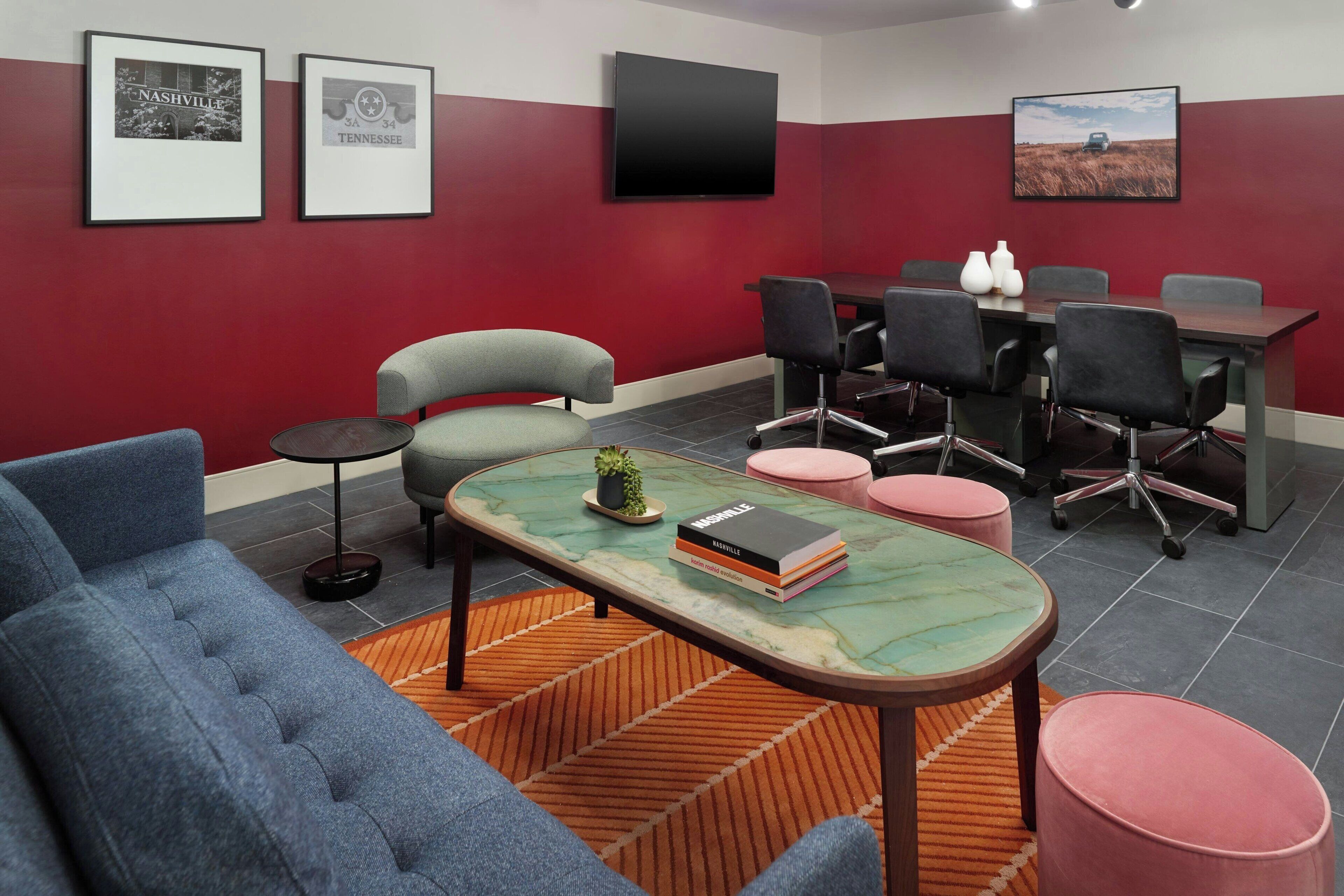 A conference room with a red and white color scheme, a large table with chairs, a television mounted on the wall, and framed pictures on the wall.