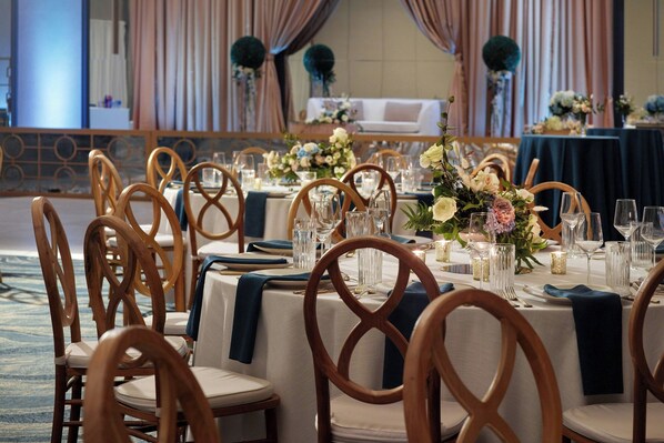 Un salón de banquetes con mesas redondas, sillas de madera y centros de mesa florales.