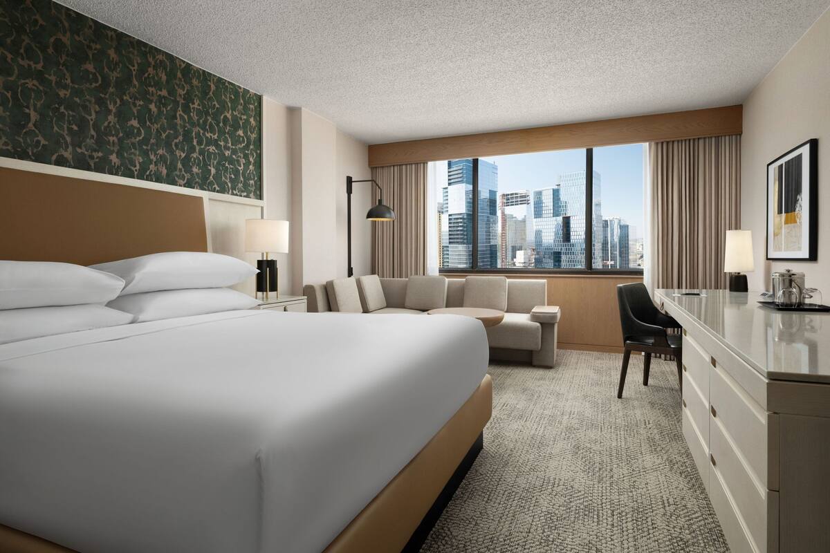 Une chambre d’hôtel moderne dotée d’un grand lit, d’un canapé, d’un bureau et offrant une vue sur le panorama urbain.