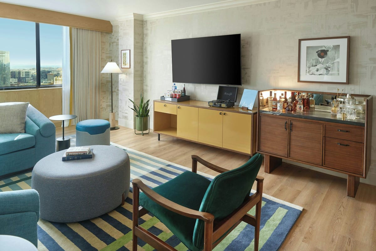 Un salon moderne doté d’un grand téléviseur à écran plat, d’un canapé, d’un fauteuil vert, d’une table basse et d’un coin bar avec des bouteilles.