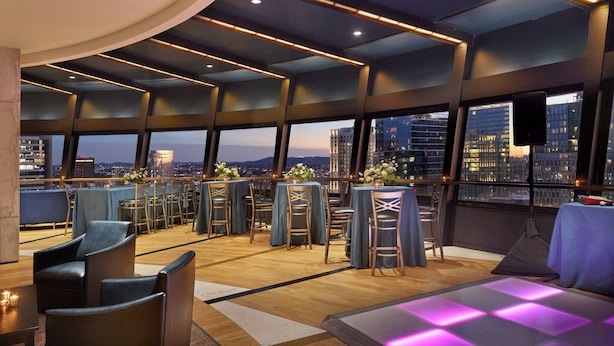 Ein moderner Lounge-Bereich mit Sitzgelegenheiten und Tischen, große Fenster mit Blick auf die Stadt und ein gestreifter Boden.