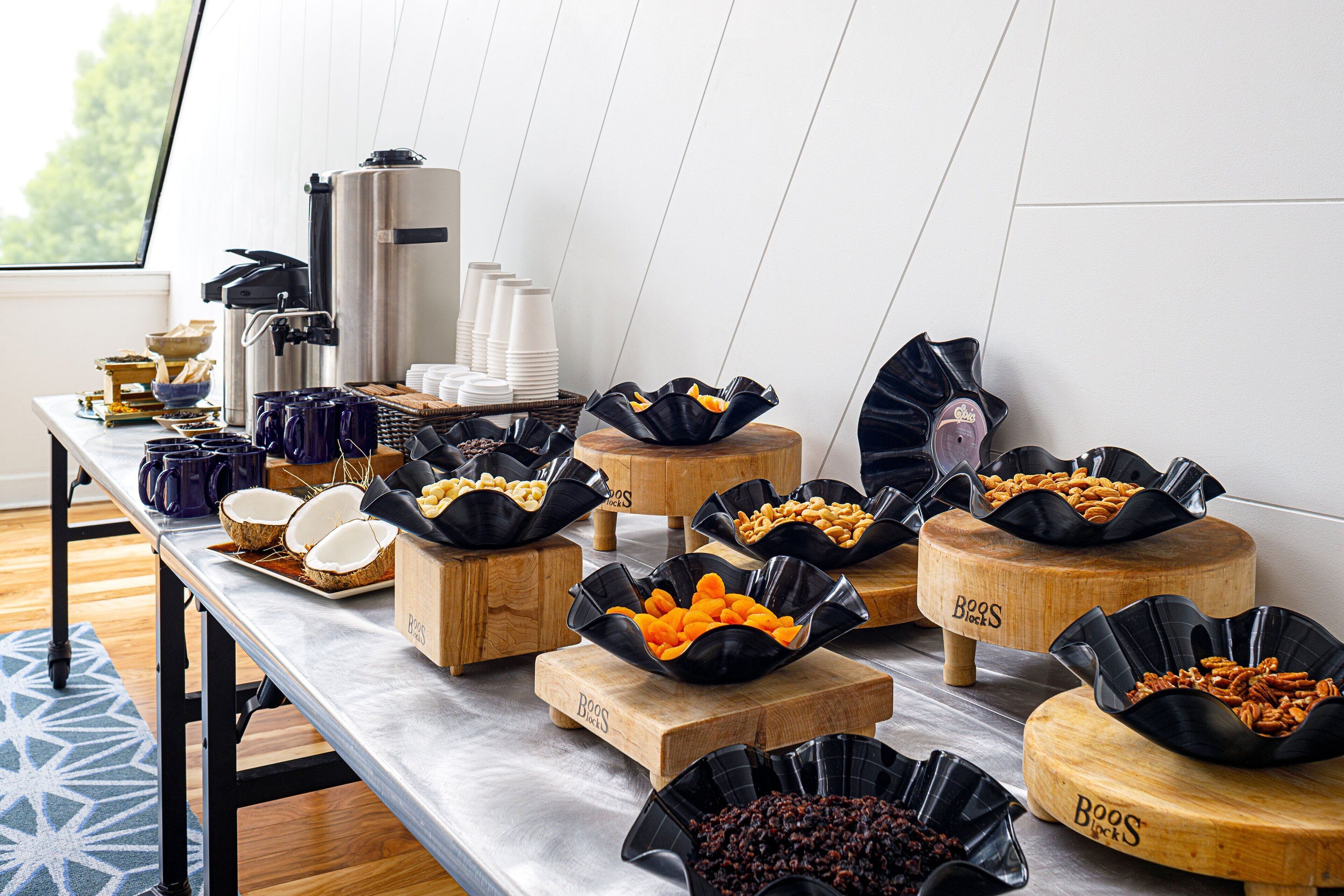 A buffet table with various food items in black bowls, a coffee machine, and stacked white cups.