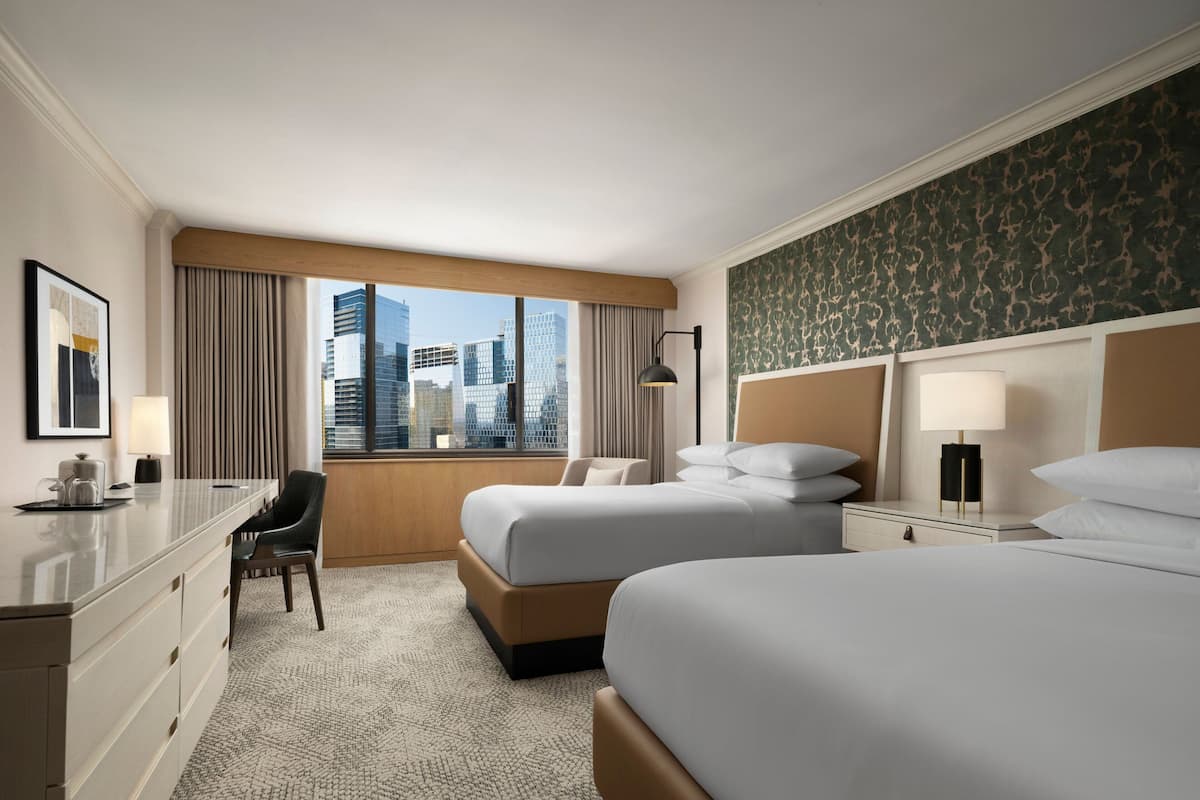Une chambre d’hôtel avec deux lits, un bureau, une chaise et une vue sur le paysage urbain.