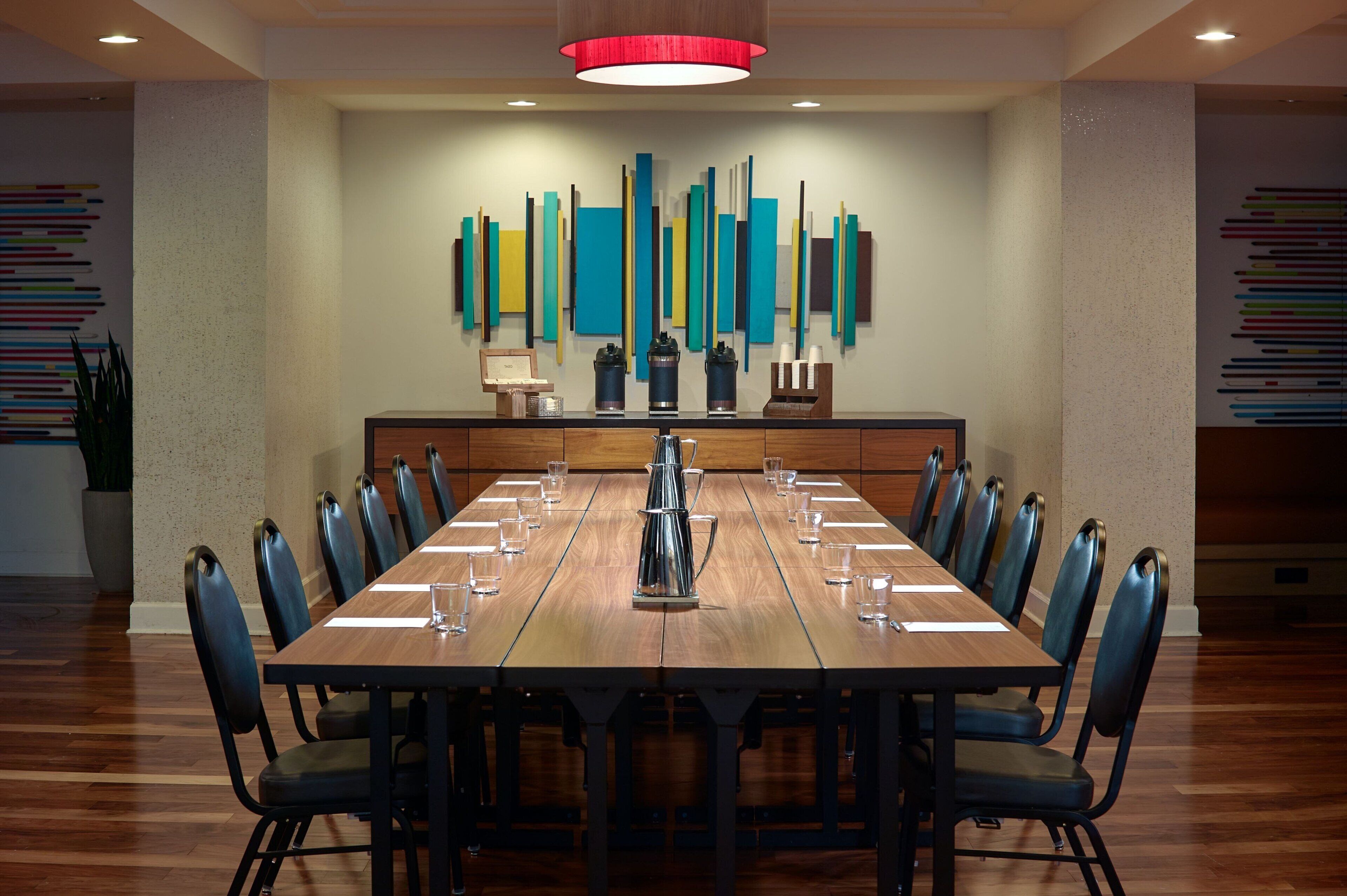 Une salle de conférence équipée d’une longue table, de chaises, d’un coin café et d’un mur décoré d’œuvres d’art moderne.