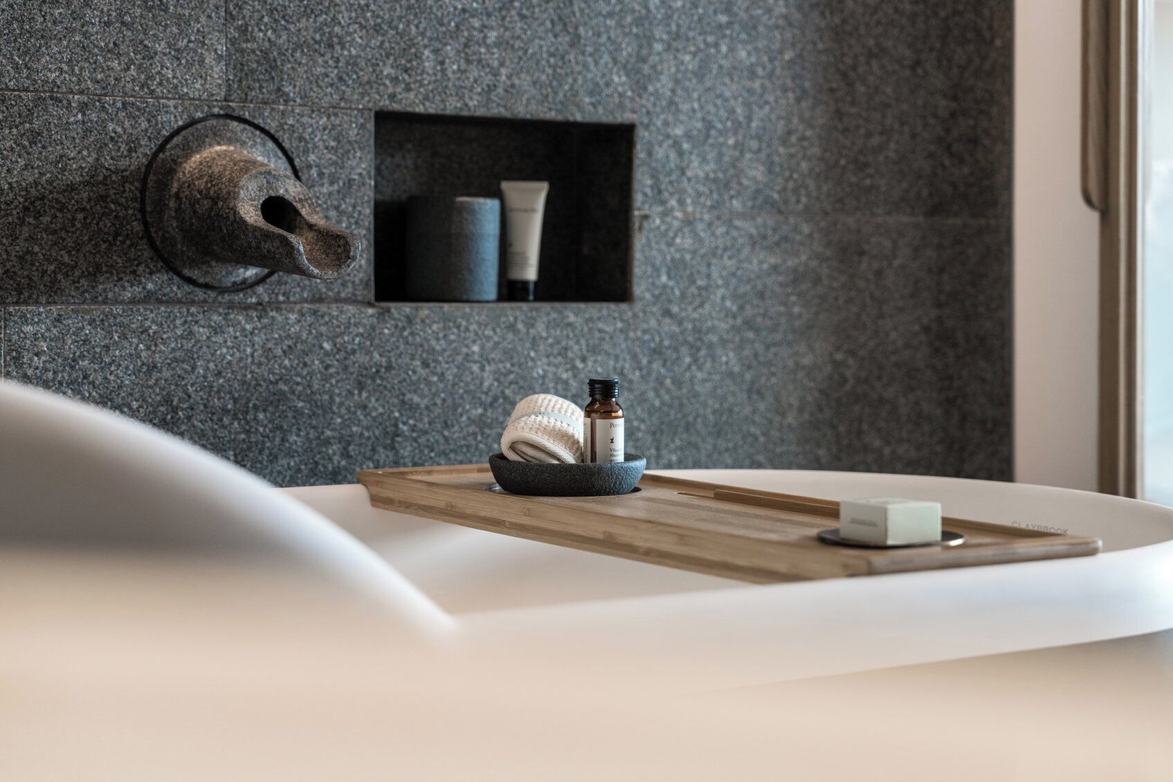 A bathroom with a stone wall, a towel, a soap dish, and a bottle of lotion on a wooden tray.