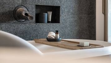 A bathroom with a stone wall, a towel, a soap dish, and a bottle of lotion on a wooden tray.
