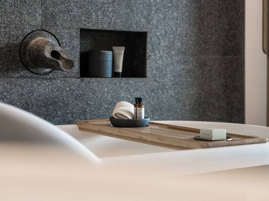 A bathroom with a stone wall, a towel, a soap dish, and a bottle of lotion on a wooden tray.