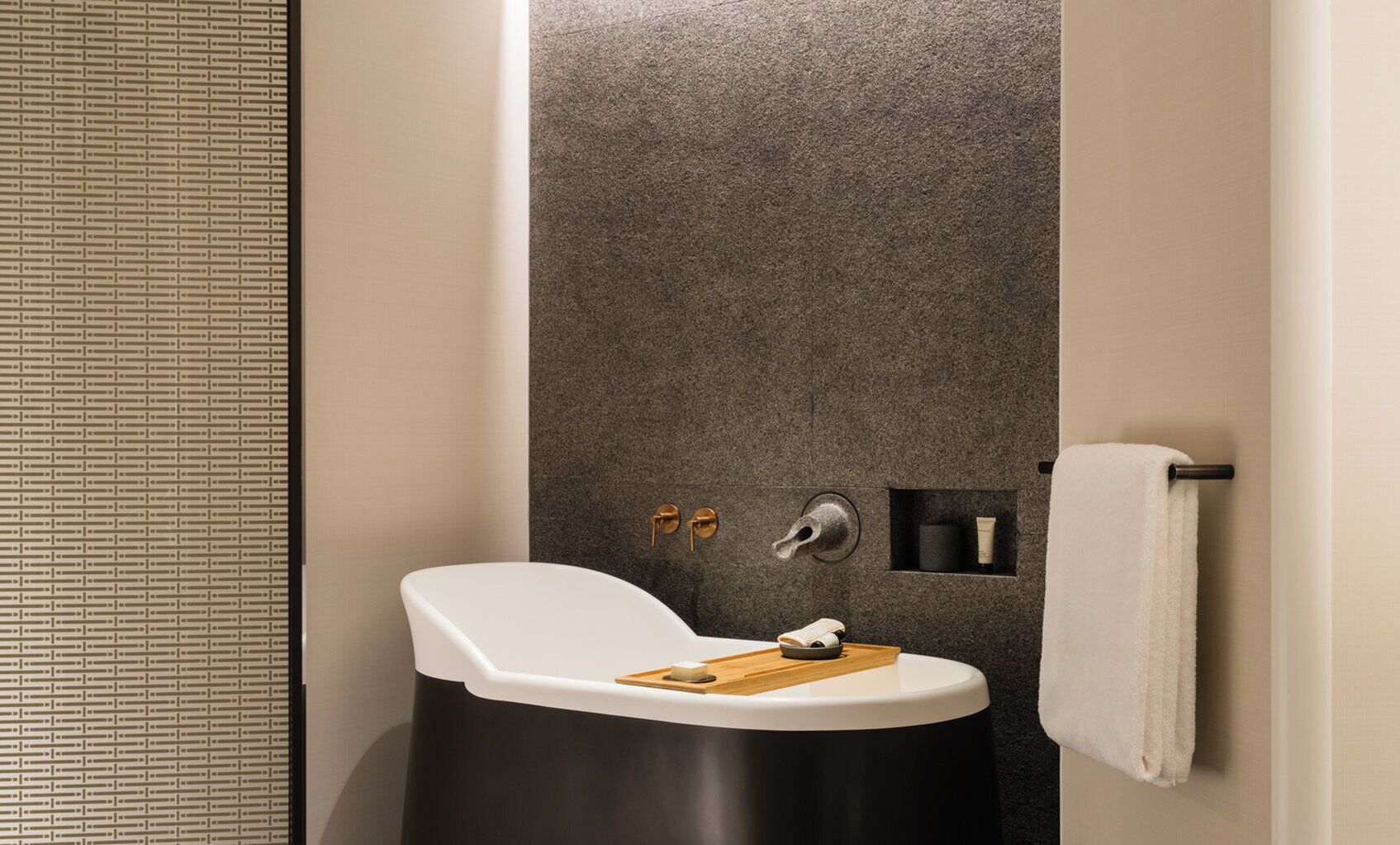A modern bathroom with a freestanding bathtub, a towel rack, and a small shelf with toiletries.