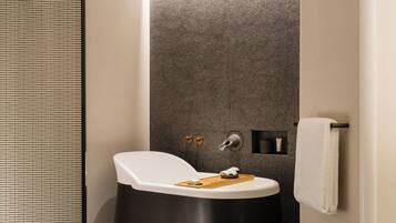 A modern bathroom with a freestanding bathtub, a towel rack, and a small shelf with toiletries.