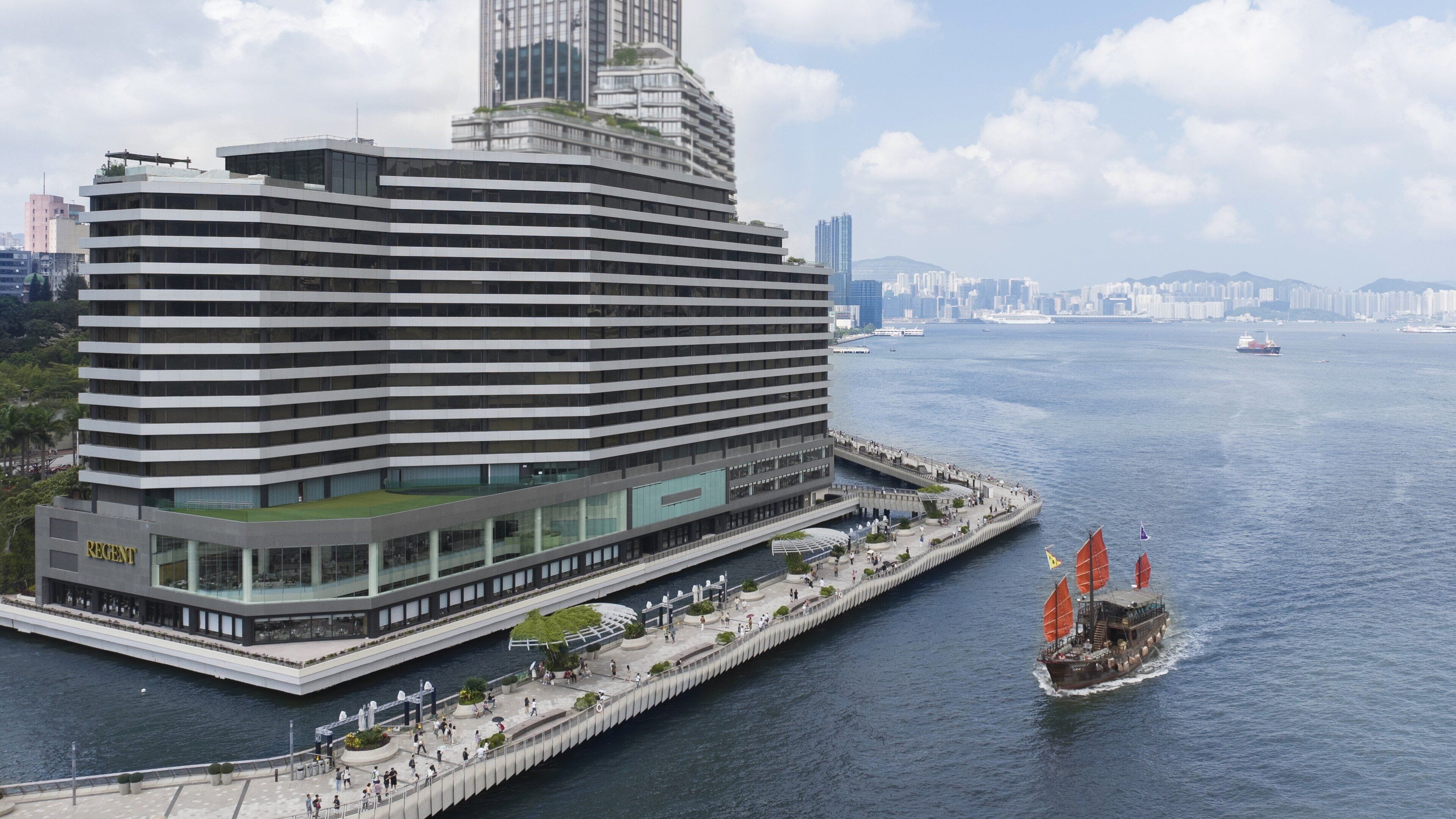 A modern hotel with a waterfront promenade, a glass facade, and a prominent 'Regent' sign.