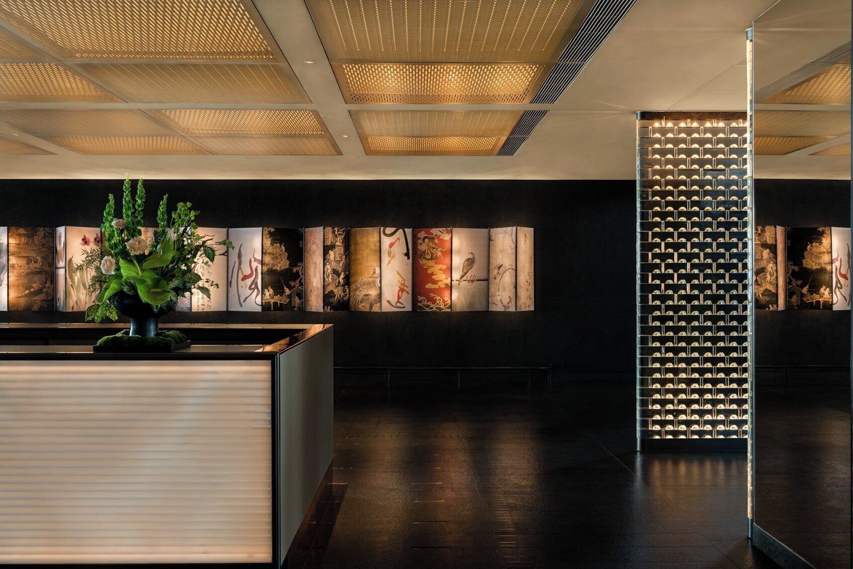 Un espace d’accueil au design moderne, comprenant un comptoir de réception, une plante décorative et une série d’œuvres d’art encadrées accrochées au mur.
