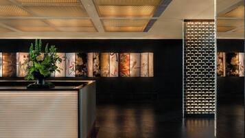 Un espace d’accueil au design moderne, comprenant un comptoir de réception, une plante décorative et une série d’œuvres d’art encadrées accrochées au mur.