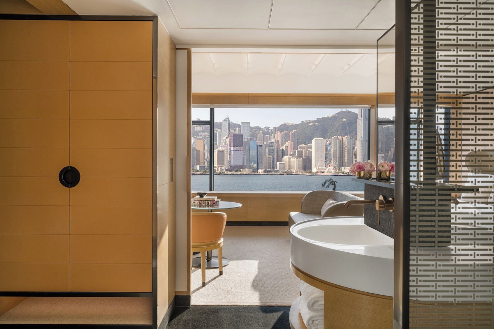 A modern bathroom with a large sink, a mirror, and a view of a cityscape through a large window.