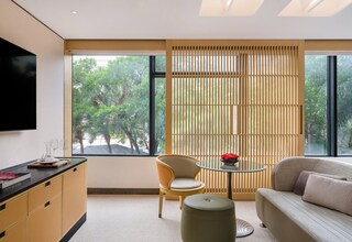 A modern living room with a sofa, a round glass table, a chair, and a TV mounted on the wall.
