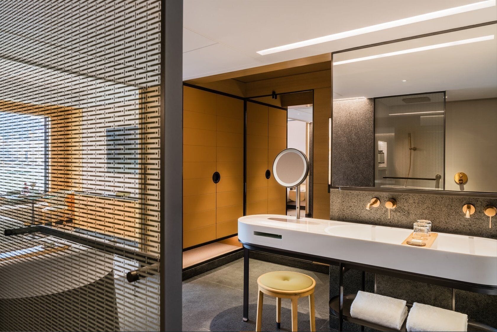 A modern bathroom with a large mirror, a bathtub, and a stool.