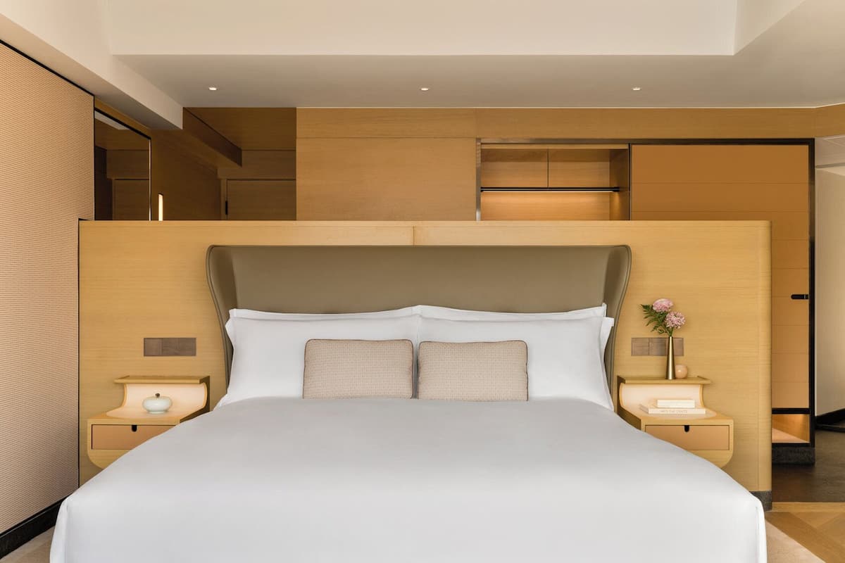 Une chambre d’hôtel moderne avec un grand lit, une tête de lit en bois et des tables de chevet intégrées.
