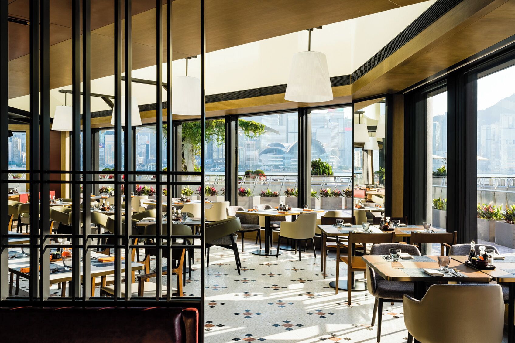 A modern restaurant with large windows, indoor plants, and a city view.